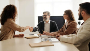 A man with gray hair shaking hands with a woman in a business meeting, indicating successful recruitment.
