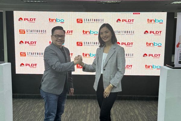 Two individuals shake hands in front of a screen displaying logos of Staffhouse, PLDT Global, and tinbo.