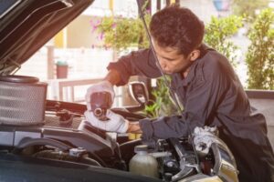 Mechanic working under a car hood with a power tool.