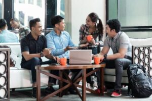 Group of colleagues having a casual discussion around a coffee table with a laptop and mugs.