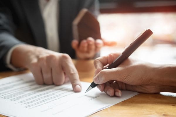 Person signing a contract with another person pointing at the document.