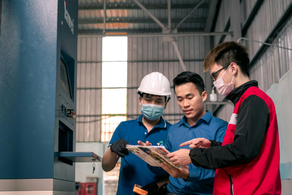 Three men wearing protective gear review a magazine about skill sourcing for the construction industry in Qatar.