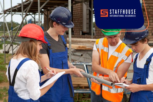 Three individuals wearing hard hats and overalls pose in front of a construction site, showcasing their work environment.