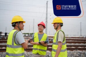 Three men in safety vests discussing plans while standing on railroad tracks.