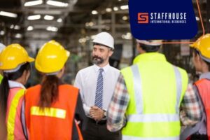 Supervisor briefing workers wearing safety helmets and vests in a factory