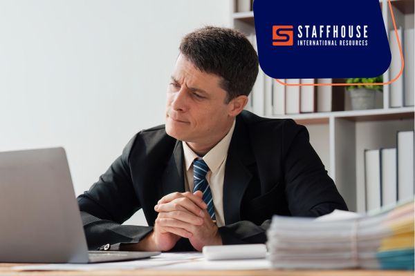 A man dressed in a suit is at a desk, engaged with his laptop in a corporate workspace.